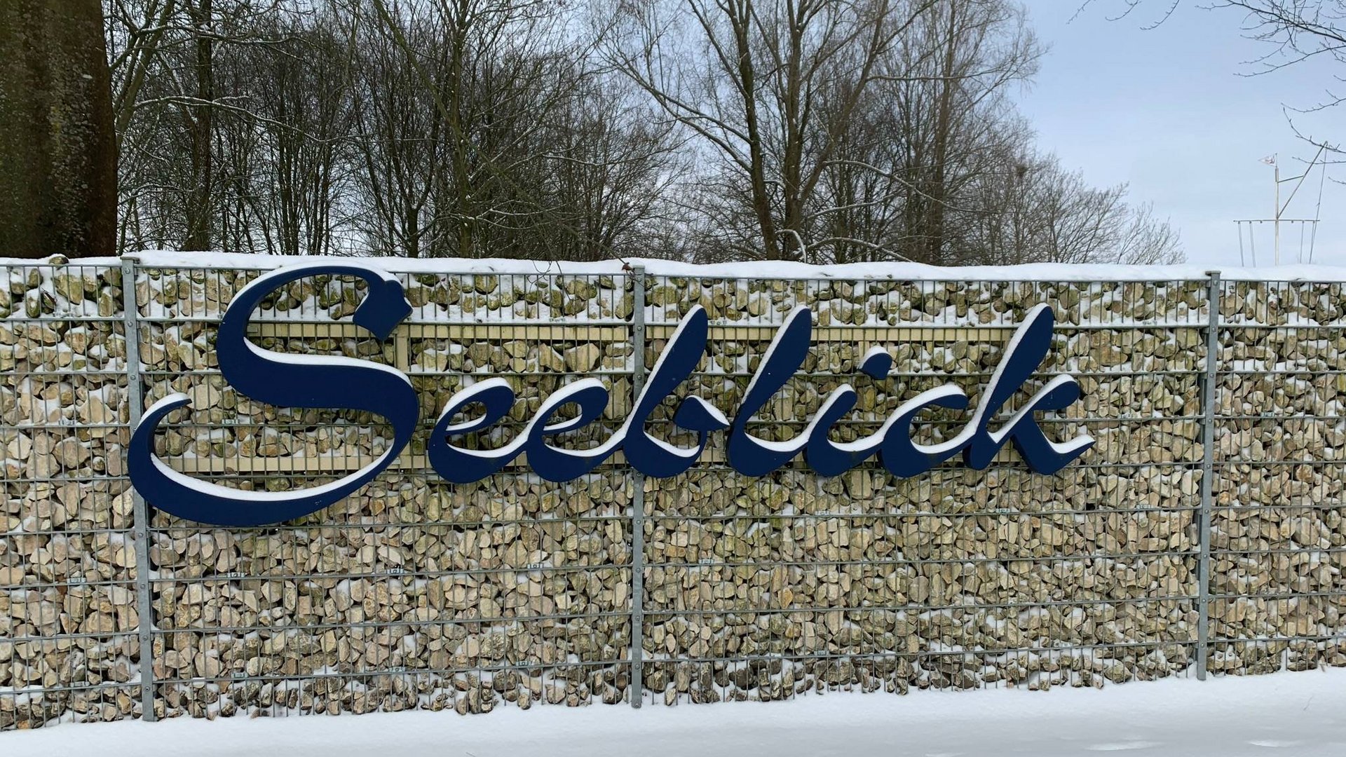 Urlaub am See in NRW - sogar im Winter wunderschön! Metallschild mit dem Wort Seeblick an Gabionenwand im Schnee