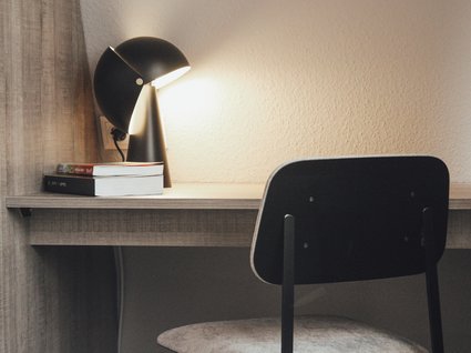 Aparthotel am See in Gronau Schreibtisch mit Lampe, zwei Büchern und einem Stuhl in einem einfachen Raum