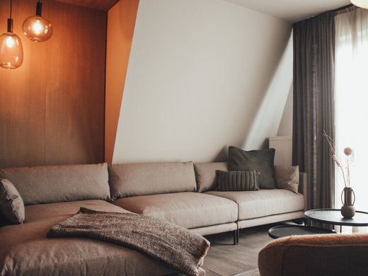 Unsere Appartements am See Gemütliches Wohnzimmer mit grauem Sofa, Beistelltischen und dekorativer Vase