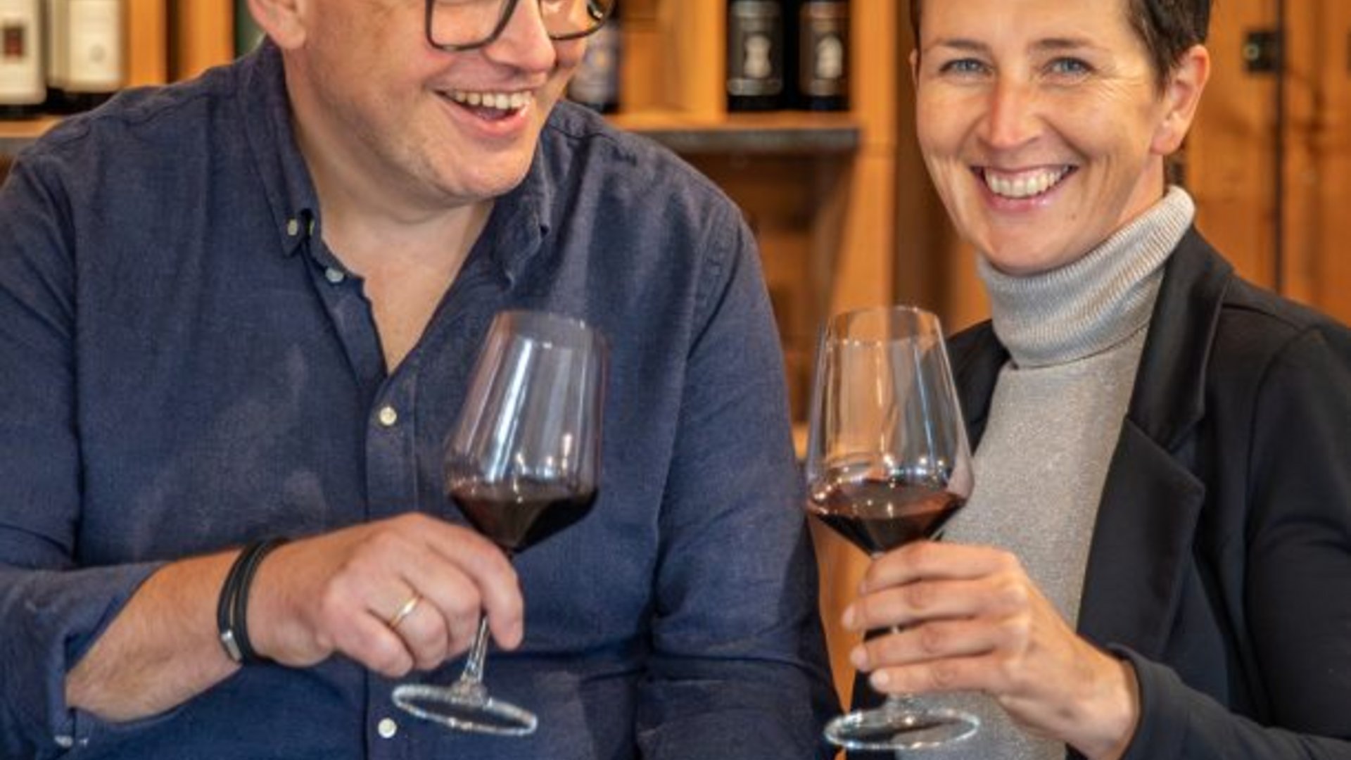 Kurzgeschichten und Weingeflüster Lächelndes Paar stößt mit Rotwein in einem Weingeschäft an