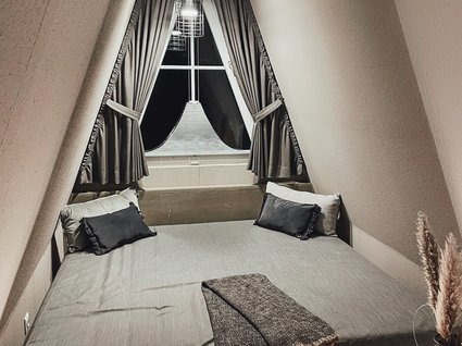 Aparthotel am See in Gronau Gemütliches Bett im spitz zulaufenden Raum mit Vorhängen und Beleuchtung