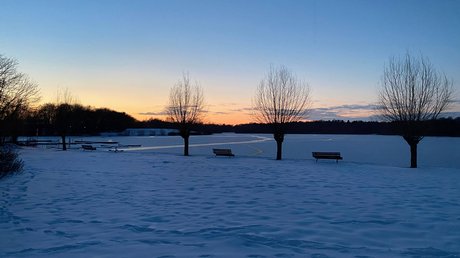 Appartementhotel Seeblick: Bildergalerie Verschneiter Park mit Bänken und kahlen Bäumen bei Sonnenuntergang