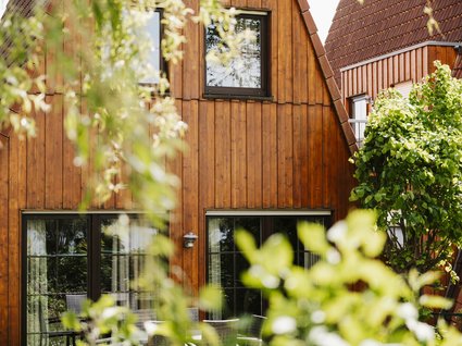 Urlaub im Apartment mit Seeblick Holzhaus mit großen Fenstern und grünen Pflanzen im Vordergrund