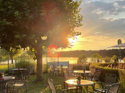 Aparthotel am See in Gronau Leerer Garten mit Tischen und Stühlen bei Sonnenuntergang am See