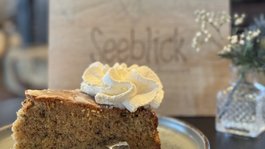 Seeblick: Urlaub am See in NRW Ein Stück Kuchen mit Sahne auf einem Teller mit Blick auf ein Holzschild mit Schrift