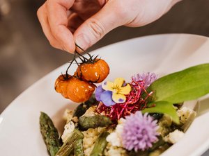 Restaurant Seeblick: Speisekarte Hand legt gegrillte Kirschtomaten auf Spargelgericht mit essbaren Blumen
