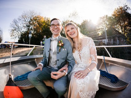 News vom Hotel direkt am See in NRW Glückliches Brautpaar in Hochzeitskleidung sitzt in einem Boot im Sonnenlicht