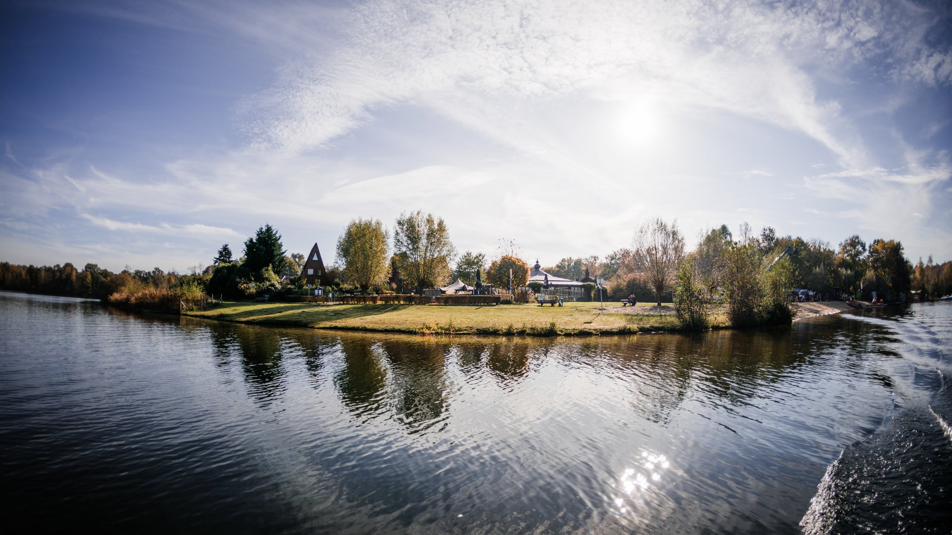 Erholung, Abenteuer und Badespaß für die ganze Familie – direkt am Dreiländersee Insel mit Bäumen und Häusern am ruhigen See unter bewölktem Himmel