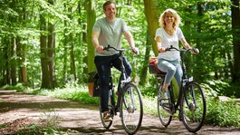 Seeblick: Urlaub am See in NRW Glückliches Paar fährt Fahrrad auf Waldweg bei Sonnenschein