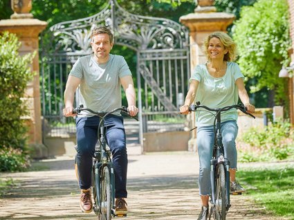 Seeblick: Urlaub am See in NRW Lächelndes Paar fährt bei sonnigem Wetter auf Fahrrädern entlang eines Weges