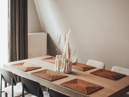 Unsere Appartements am See Moderner Esstisch mit sechs Stühlen und dekorativer Vase mit Trockenblumen