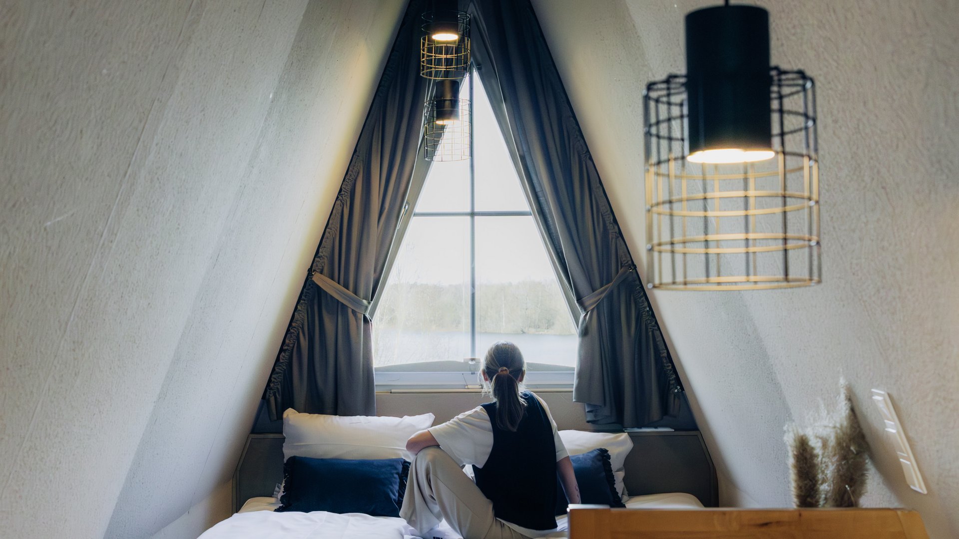 Seeblick Gronau: Urlaub inmitten der Natur Person sitzt auf einem Bett in einem gemütlichen Dachzimmer mit Fenster