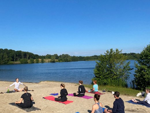 Seeblick Gronau: Urlaub inmitten der Natur Menschen praktizieren Yoga am Strand eines Sees bei klarem Himmel