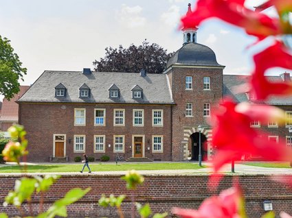 Seeblick Gronau: Urlaub inmitten der Natur Rotes Backsteingebäude mit gewölbtem Turm vor blauem Himmel und Blumen im Vordergrund